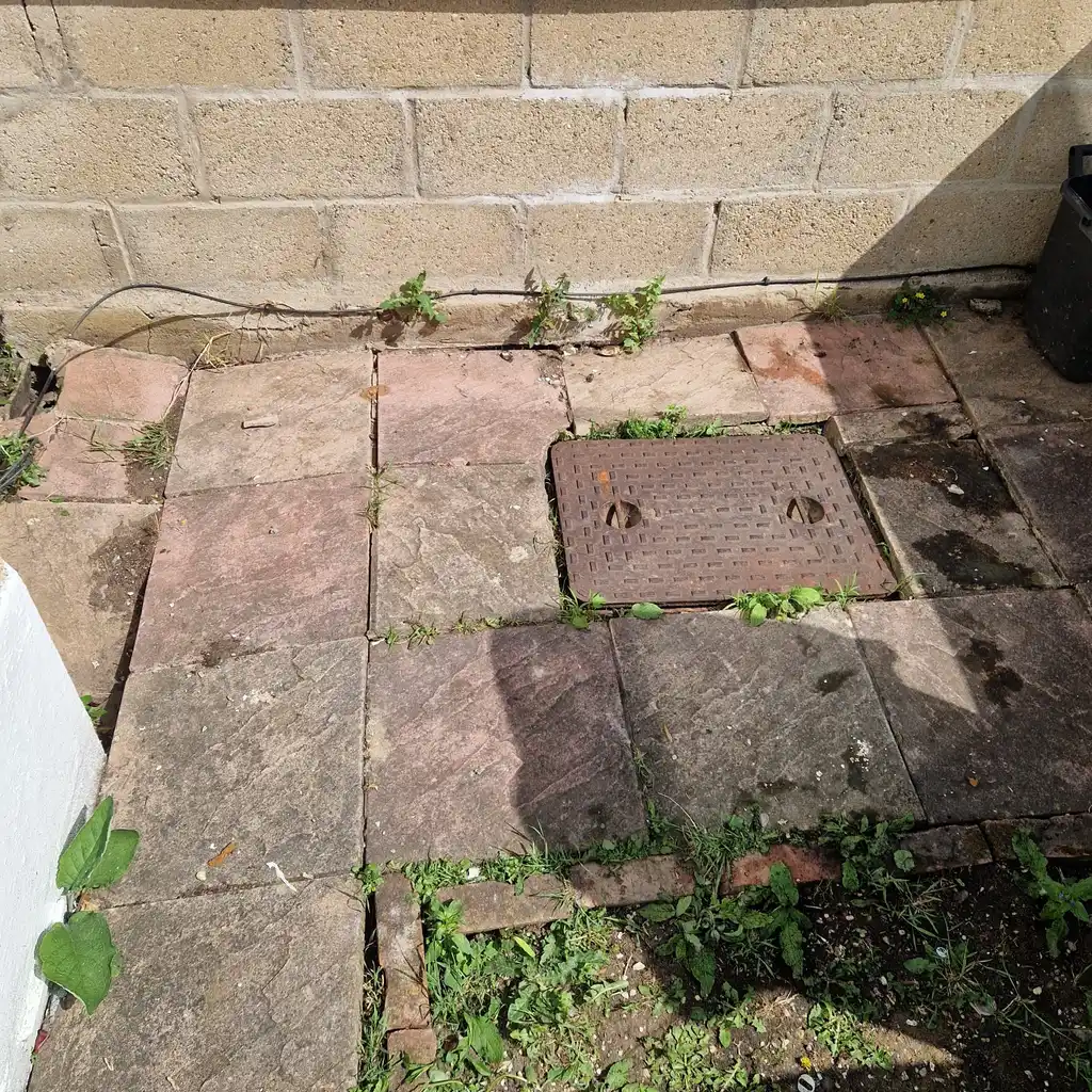 Manhole cover set into a patio showing reinstatement work after drain excavation