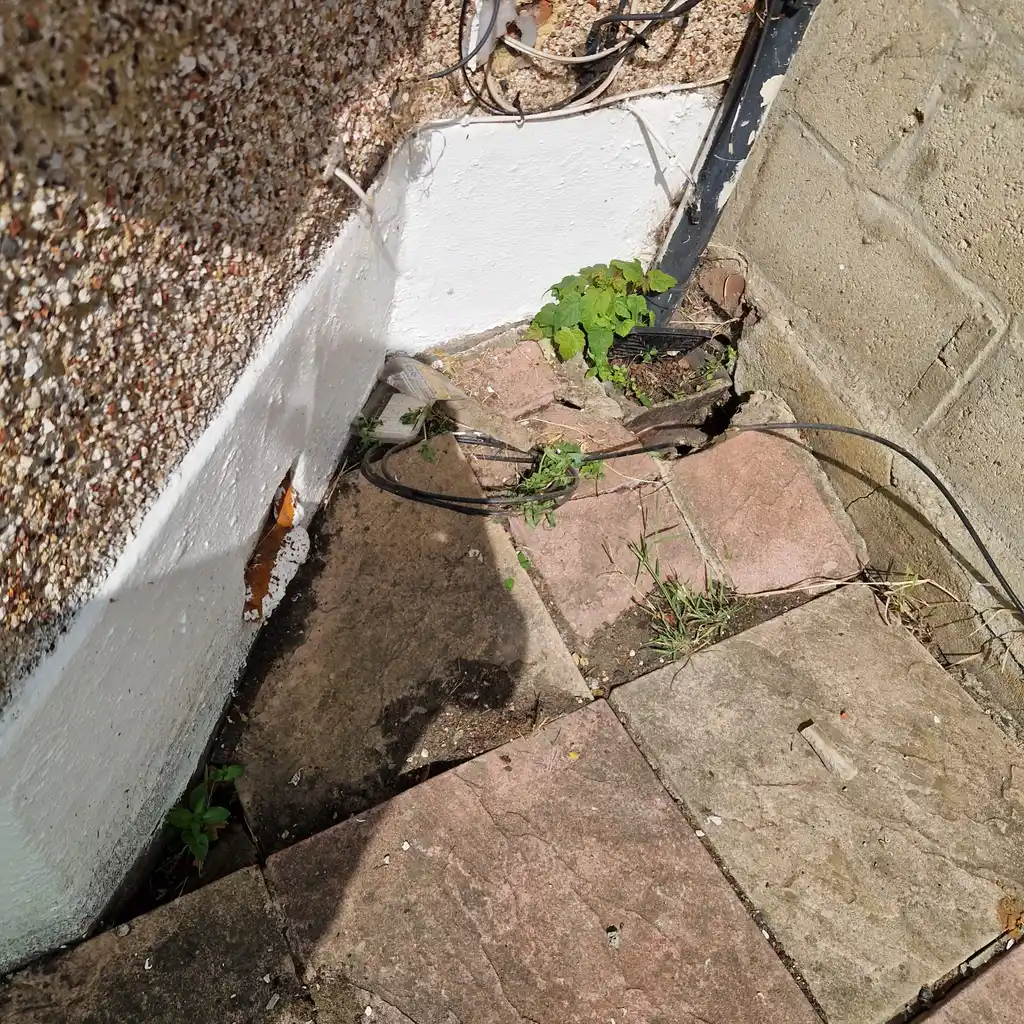 Engineer locating overgrown drain gully hidden by weeds at Erith property corner