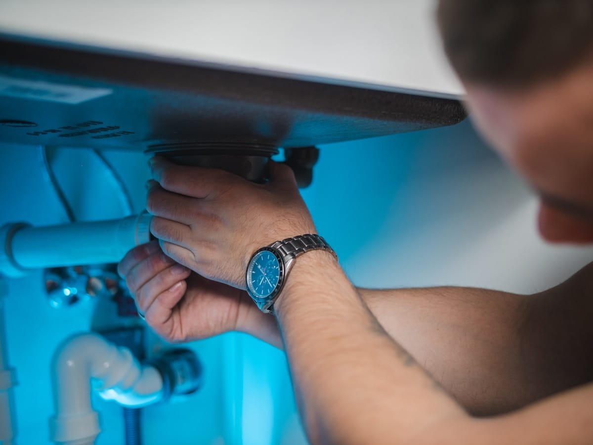 Plumber fixing a pipe under a kitchen sink during a blocked drain repair