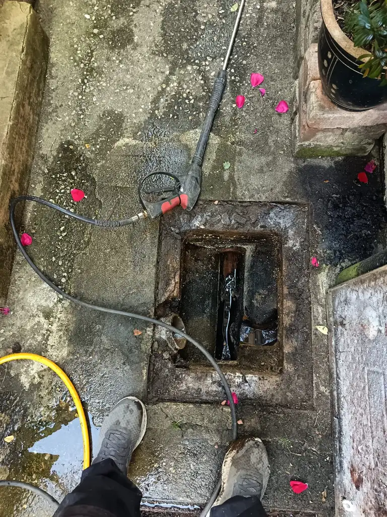 Engineer using pressure jetting equipment near a drain chamber during a collapsed drain repair