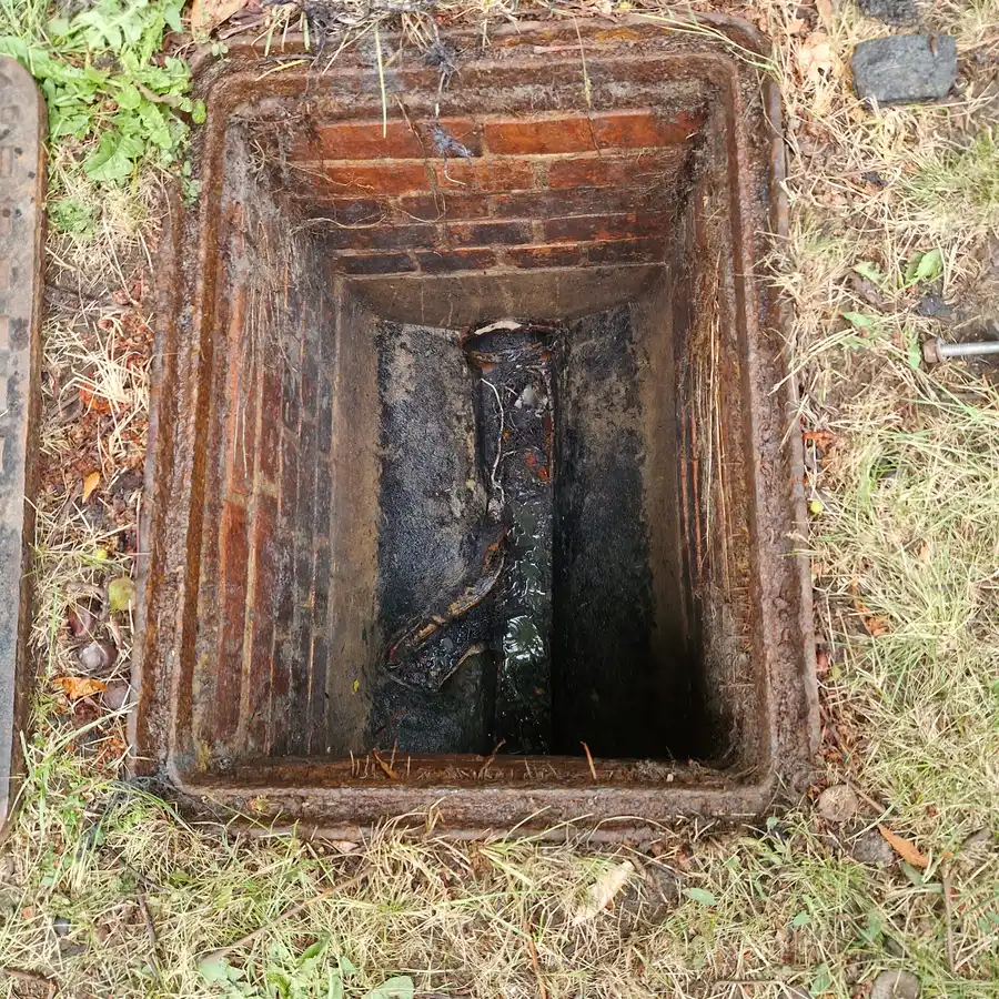 Brick inspection chamber with silt and debris lining the channel, typical of older Chiswick drainage